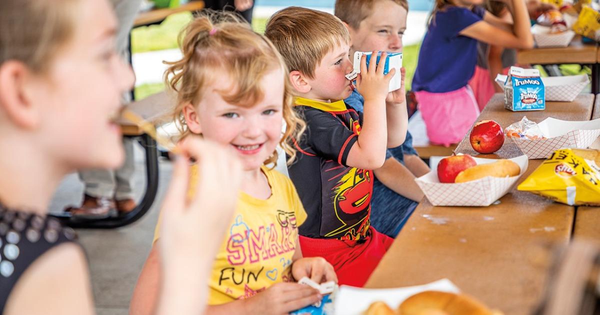 Jax Roberts, center, enjoys a refreshing swig of milk, while his cousin, Lilyana Weil, flashes a grin during a free picnic lunch provided by local schools and area partners through a summer feeding program at a Bismarck park.   “It’s usually just one person at the school who sees the application, but that might be just enough to deter families,” she says.  In some cases, pride is the reason households choose not to complete a free and reduced price meal application. But Schloer and Egeland agree that the ch